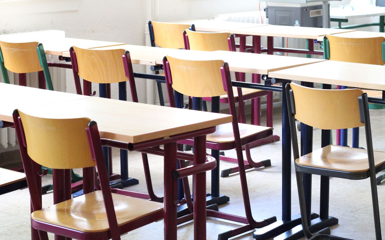 An empty classroom in daylight with rows of wooden desks and chairs
