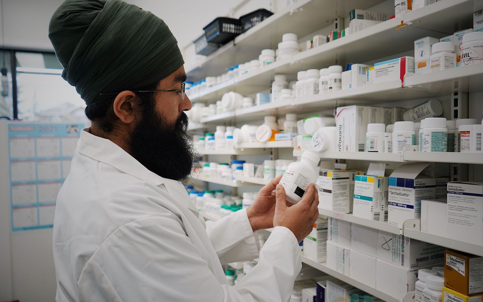 A pharmacist checking a medicine bottle in front of stocked shelves